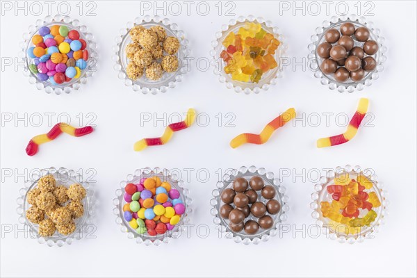 Sweets on and next to small glass plates in rows on a white background photographed from above