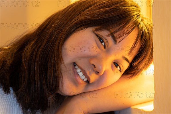 Portrait of young Japanese woman smiling and looking at camera on yellow background with romantic expression