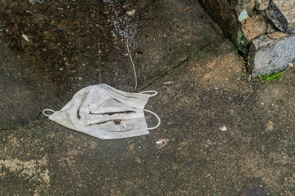 Dirty wet medical face mask laying on sidewalk next to puddle of water