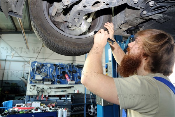 Symbolic image: Motor vehicle mechatronics technician inspects a car on the lift