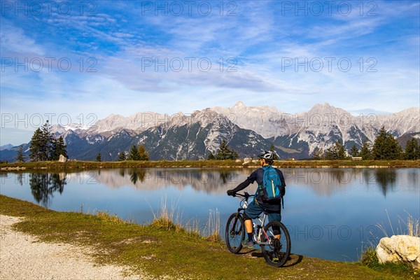 Mountain biker taking a break at the Kaltwassersee lake in Seefeld/Tyrol. The snow-covered peak on the left of the picture is the Zugspitze