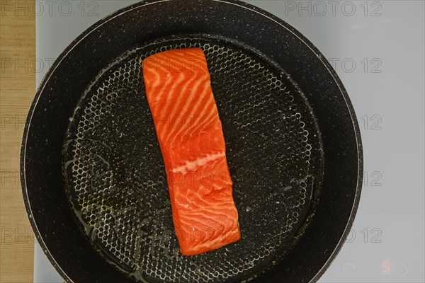 Top view of piece of fresh trout steak in a frying pan on electric stove
