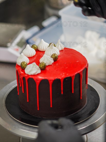 Rich chocolate cake covered with red glaze and adorned with meringue kisses and gold painted dark chocolate balls and sweets