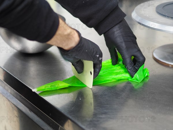 Pastry chef preparing a filling pastry bag with vibrant green frosting in a commercial kitchen