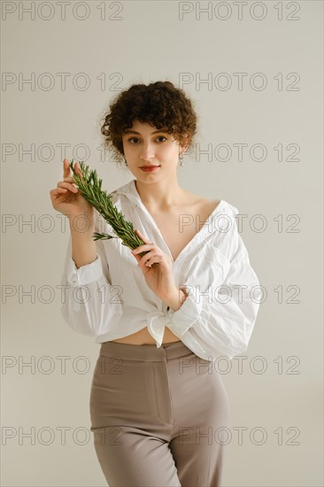 Young woman wearing a loosely tied white blouse shows a long branch of rosemary