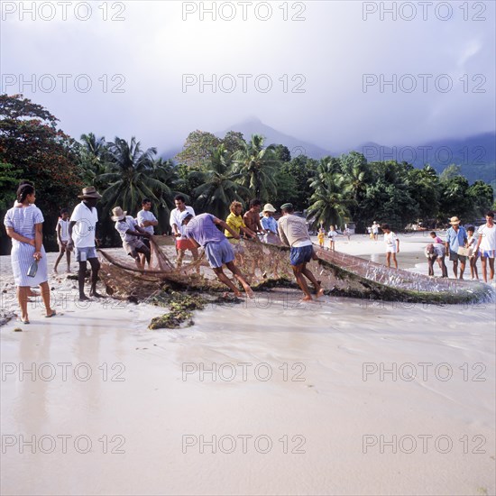 Seychelles, Mahe, Beau Vallon, fishermen pull fishing net ashore, Africa