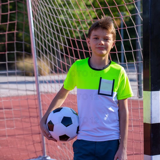 Symbolic image: Ten-year-old boy on a football pitch proudly holding a football in his arms