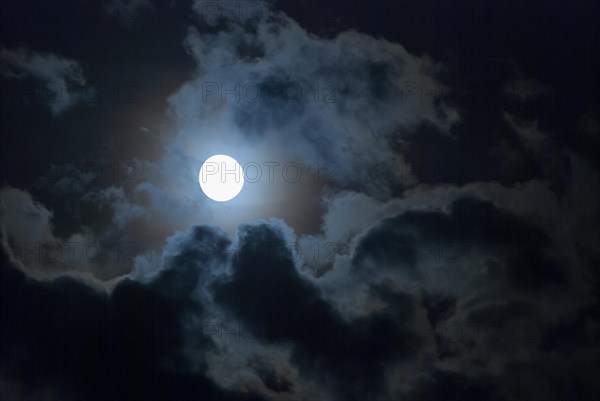 The full moon shines brightly in a cloudy, stormy, black sky and has a halo (corona), fairytale-like, mystical night shot, dark, somewhat creepy mood, ghostly, symbolic image for fear, nightmare, horror, fantasy, motion blur, wiping effect, Mecklenburg-Western Pomerania, Germany, Europe