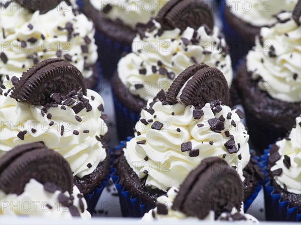 Close-up of a large group chocolate cupcakes with white cream frosting and dark chocolate cookie topping