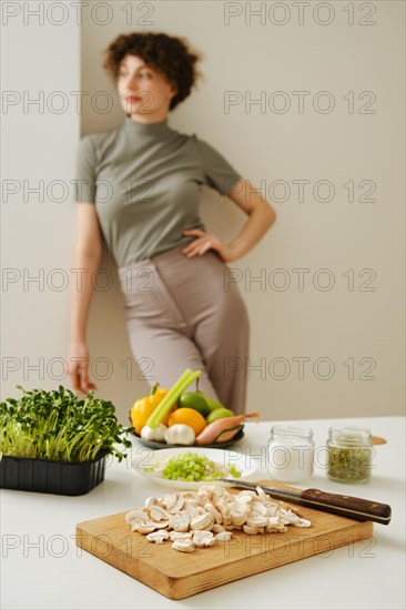 Kitchen table with fresh organic vegetables and blurred young woman on background leaning against the wall