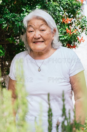 Portrait of a white-haired elderly woman of Japanese ethnicity smiling and looking at the camera in the garden of her home