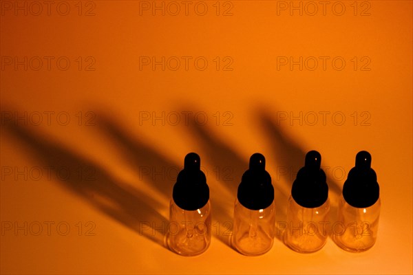 Four glass eye dropper bottles with dark black shadows on golden orange background. A little noise added for effect