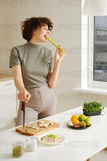 Cute woman bites a stalk of celery while preparing meal