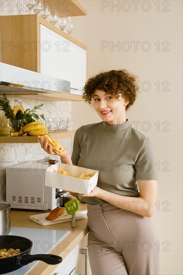 Smiling woman takes pappardelle pasta out of cardboard box