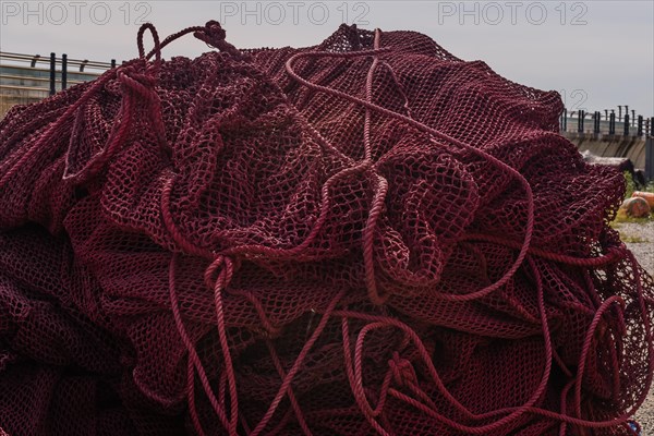 Closeup of large ball of maroon colored fishing nets in front of sea wall on cloudy day in South Korea