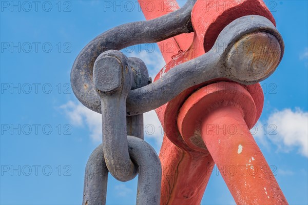 Closeup of linchpin attached to large red anchor with blue cloudy sky in background in Yeosu, South Korea, Asia