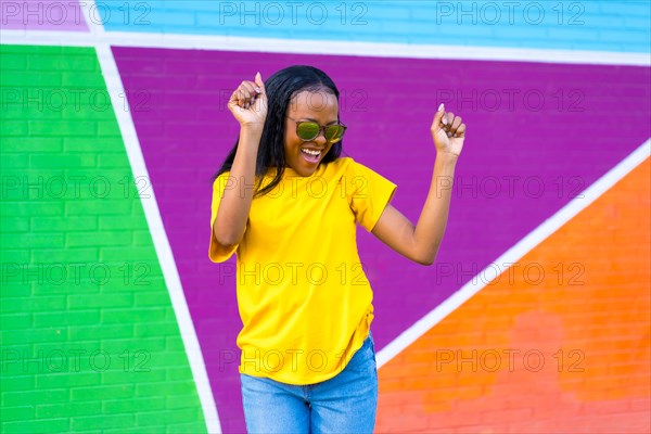 Frontal portrait of a young and happy african woman smiling and dancing next to colorful wall