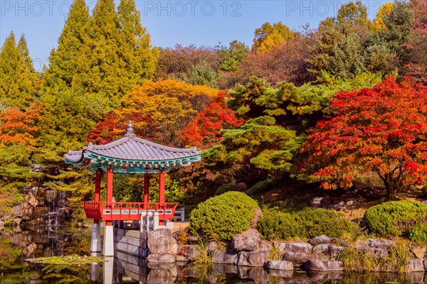Beautiful oriental gazebo with terracotta tile roof at edge of man made pond with small waterfall in background in South Korea