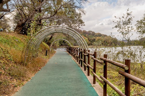 Metal trellis over green paved hiking trail at lakeside park in South Korea