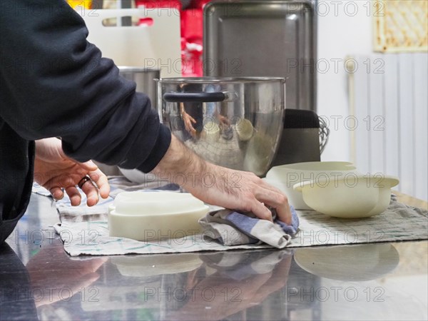 Person cleaning a countertop next to bowls and a blender in a kitchen environment