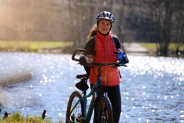Attractive mountain biker stands with her mountain bike in front of a lake