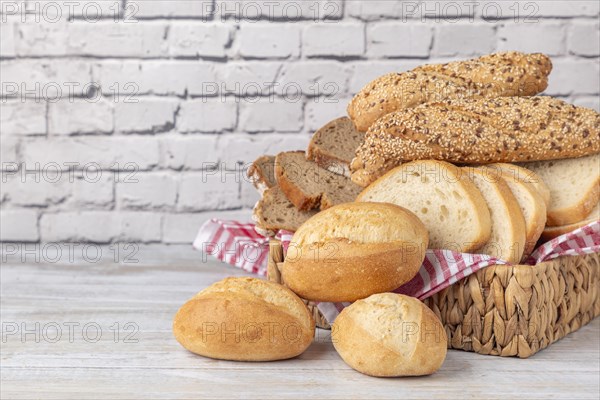 Various types of bread and pastries in a basket on a wooden table in front of a white brick wall, copy room