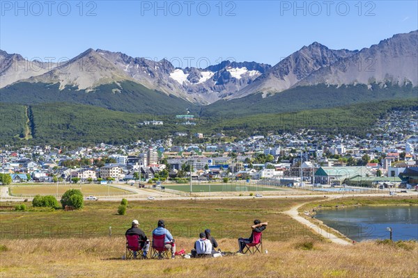 A family sits in chairs in a meadow with a view over the city of Ushuaia and the mountains Cerro Martial and Cerro del Medio, Ushuaia, Tierra del Fuego Island, Patagonia, Argentina, South America