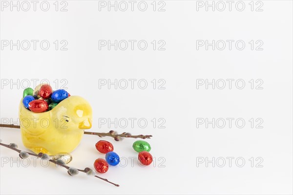 Colourful chocolate eggs in yellow ceramic chick next to palm kitten, white background, copy room