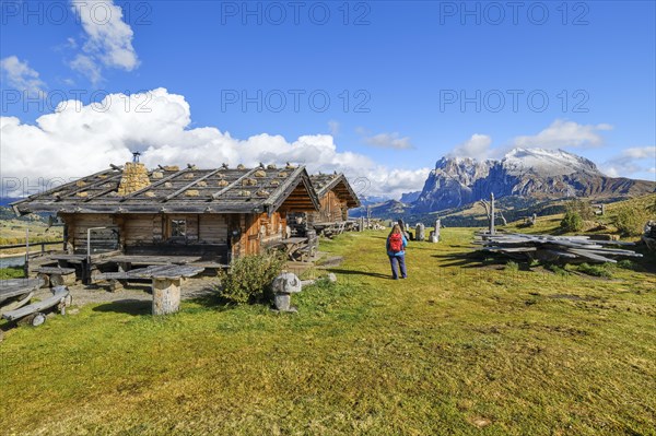 Edelweiss hut on Alpe di Siusi, hiker with red rucksack, Sassopiatto and Sassolungo, clouds, Dolomites, South Tyrol