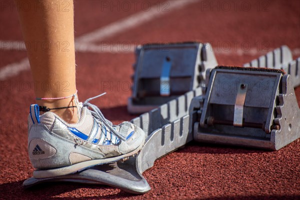 Young track and field athlete with Adidas spikes at the starting block in front of a sprint