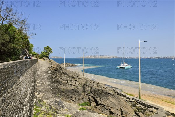 Fortified coast with catamaran in front of rocky shore in Dinard, Ille-et-Vilaine, Brittany, France, Europe