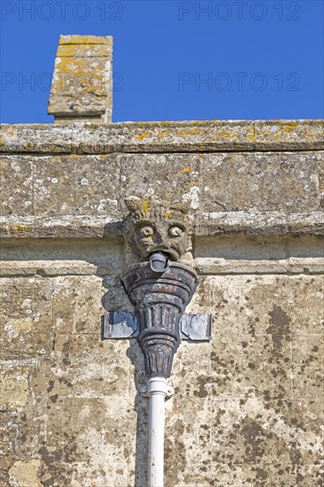 Gargoyle grotesque face drainpipe on wall medieval church of Saint John, Inglesham, Wiltshire, England, UK