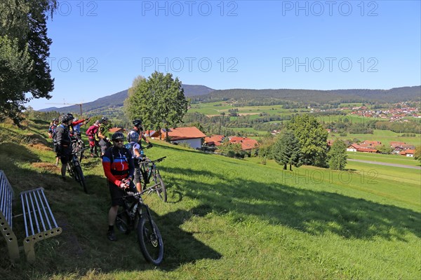 Mountain bike tour through the Bavarian Forest with the DAV Summit Club: short break in a meadow paths towards Arrach. In the background, the summit of the Osser, a mountain on the border between Germany and the Czech Republic
