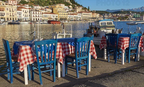 Outdoor area of a taverna with sea view, red and white tablecloths and boats, Gythio, Mani, Peloponnese, Greece, Europe