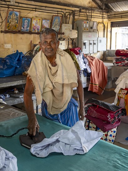 A man irons shirts with an antique iron at Dhobi Khana Public Laundry, Fort Kochi, Cochin, Kerala, India, Asia