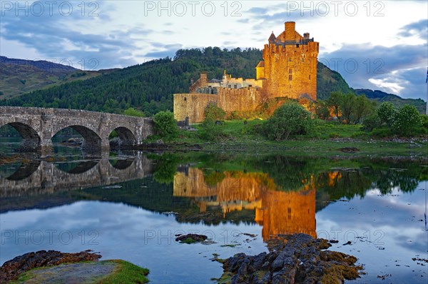 The illuminated Eilean Donan Castle is reflected in the water on a calm evening, old stone bridge, film location for James Bond, Highlander, Rob Roy, Scotland, Great Britain