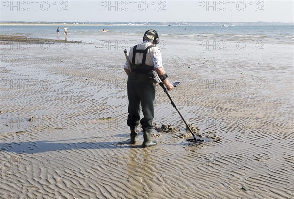 Male detectorist using metal detector at low tide, sandy beach Studland Bay, Swanage, Dorset, England, UK