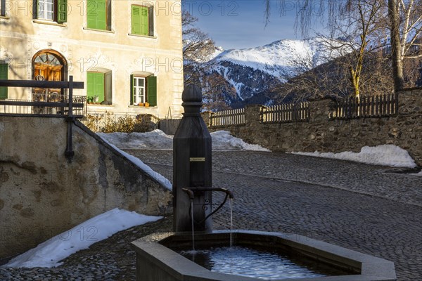Wooden fountain, house with sgraffito, facade decorations, mountain peak, snow, winter, Guarda, Engadin, Graubuenden, Switzerland, Europe