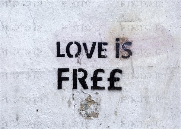 Stencilled graffito message 'Love is Free' on white wall, Newbury, Berkshire, England, UK