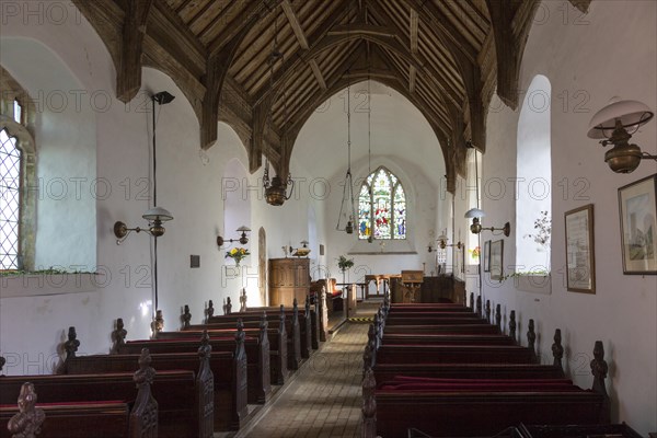Looking east down the nave towards the altar and east window with historic wooden carved pews, fine wooden roof, whitewashed walls, interior of small village parish church at South Cove, Suffolk, England, UK