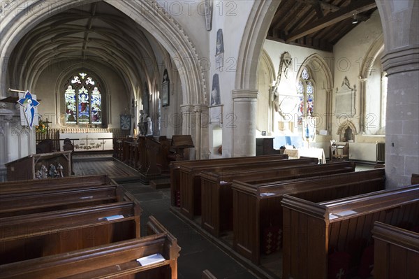 View past wooden pews through chancel arch to sanctuary and altar inside the church at Urchfont, Wiltshire, England, UK also showing side chapel in south aisle