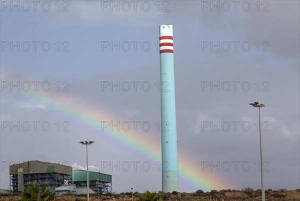 Rainbow in stormy sky behind tall blue industrial cement factory chimney, Carboneras, Almeria, Spain, Europe