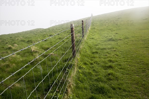 Barbed wire fence in fog on chalk downs near Knap Hill, Alton Barnes, Wiltshire, England, UK