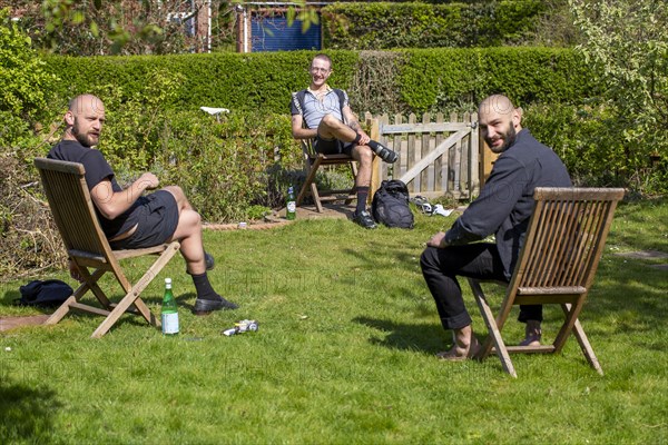 Three men having a socially distanced chat in a garden, UK during Covid-19 Coronavirus lockdown period