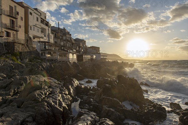 Sea water crashes against the cliffs of the rugged coastline in the town of Cefalu, Sicily, Italy, Europe