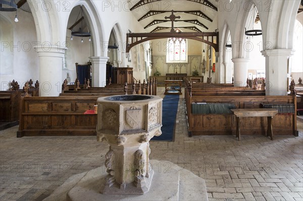 Village parish church baptismal font, Saint Nicholas, Hintlesham, Suffolk, England, UK view down wooden pews in nave to chancel and altar