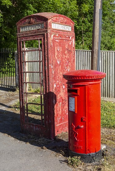 Disused vandalised red telephone box next to smart Royal Mail letter box, UK