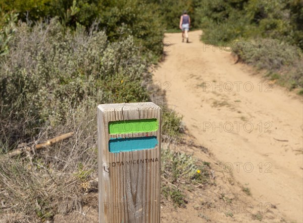 One woman walking in woodland on coastal long distance footpath trail, The Fisherman's Walk or Ruta Vicentina, near Zambujeira do Mar, Alentejo Littoral, Portugal, Southern Europe. In the foreground is the painted way mark sign for the route, Europe