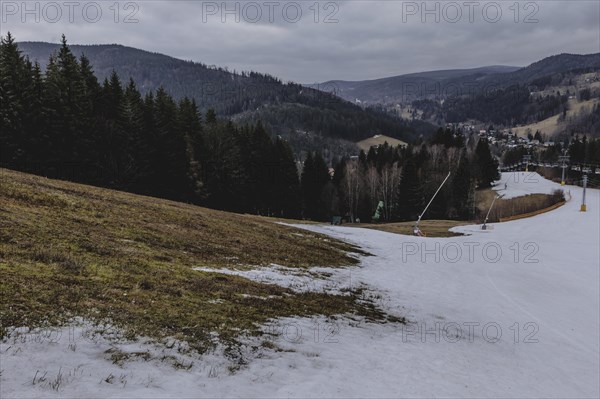 A melting ski slope next to a meadow, taken on a ski slope in the Jizera Mountains ski area near Albrechtice v Jizerskych Horach, 05.02.2024. The Czech low mountain range with its ski area is affected by increasingly warmer and shorter winters