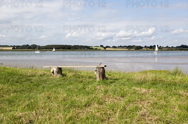 Summer landscape view of bench overlooking sailing boats on River Deben estuary, Sutton, Suffolk, England, UK